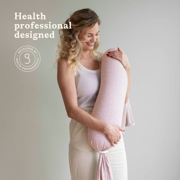 Woman holding a pink bbhugme nusing pillow with 'Health professional designed' text on a plain background