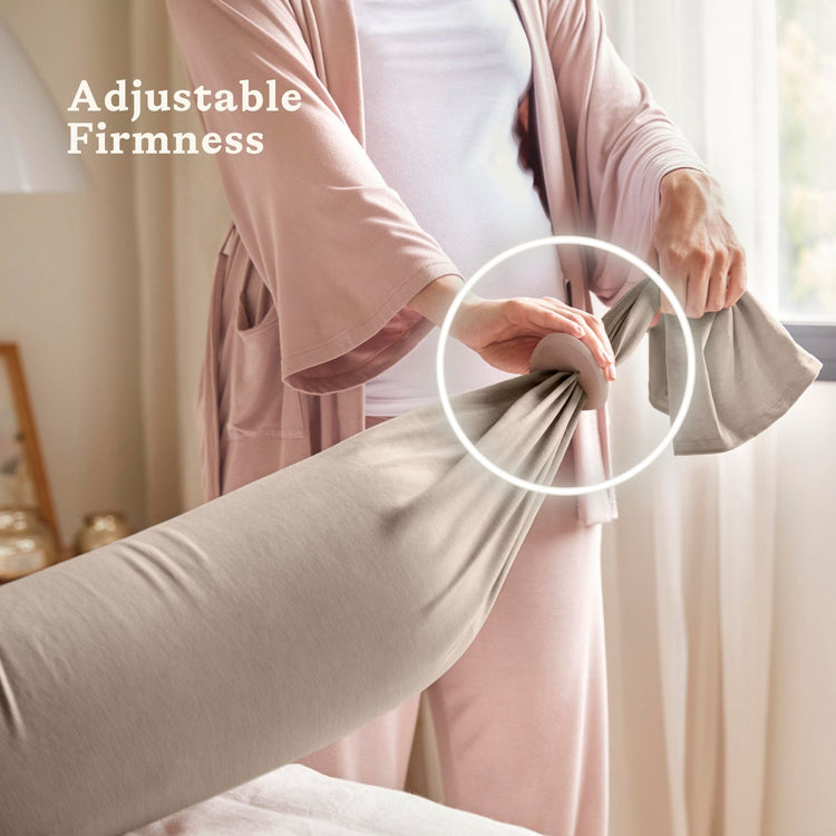 Person adjusting a beige bbhugme pregnancy pillow with text 'Adjustable Firmness' in a bedroom setting.