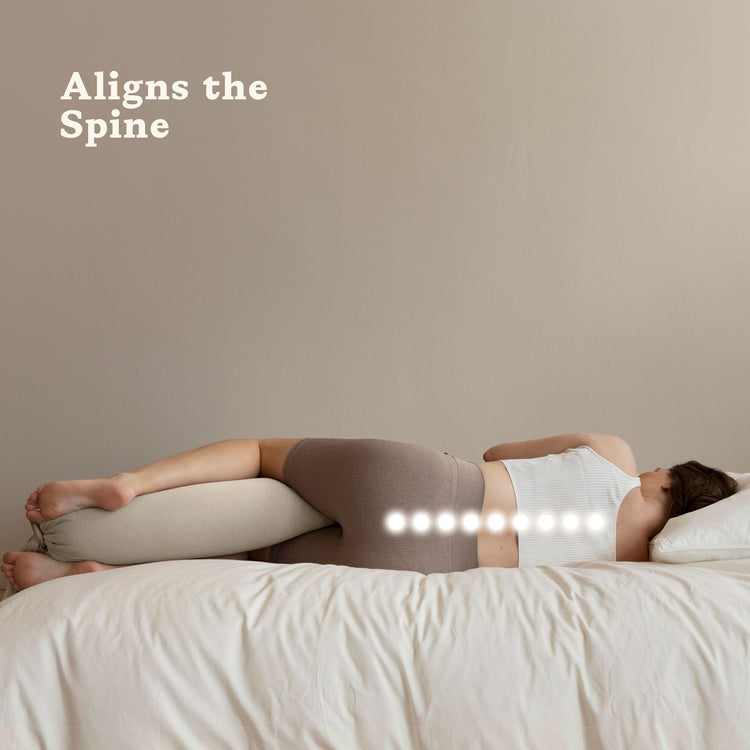 Person lying on a bed with a bbhugme pregnancy pillow 'Aligns the Spine' and a logo.